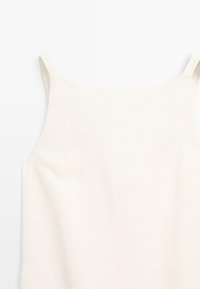 Top sans manches couleur blanc cassé en tissu lisse avec une coupe droite, présentant de fines bretelles et des détails de design minimalistes.