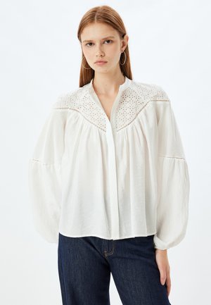 Weiße Bluse mit besticktem Detail am Einsatz, langen Puffärmeln und einer Knopfleiste. Aus leichtem Stoff mit strukturierter Oberfläche gefertigt.