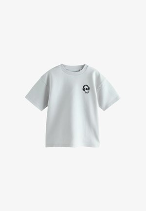 T-shirt blanc à manches courtes avec col rond, avec un petit dessin noir de crâne portant un casque audio sur la poitrine gauche.