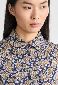 Cămașă albastră închis cu un model paisley în nuanțe de portocaliu și crem, având un guler ascuțit și închidere cu nasturi. Material neted cu un finisaj lustruit.