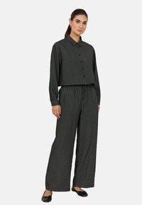 Camicia leggera a righe bianche e nere, con colletto e chiusura a bottoni, abbinata a pantaloni larghi con vita elastica.