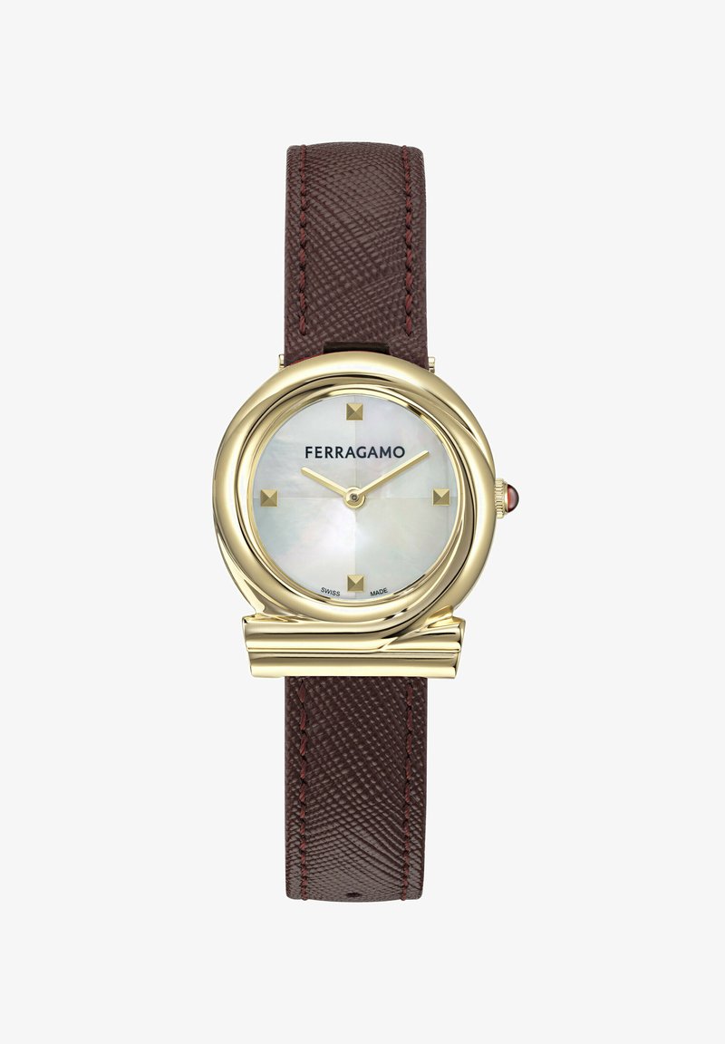 Ümmargune kell, millel on kuldtooniga korpus, emakakaunistusest valmistatud kellaplaat, pruuni tekstuuriga nahkrihm ja ruudukujulised tundemärgid. Kellal on logo kell 12 asuvas asendis.