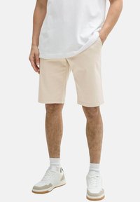 Helle beige Shorts aus einem Baumwollmix, mit seitlichen Taschen, gerader Passform und lässigem Schnitt. Kombiniert mit weißen Sneakers.