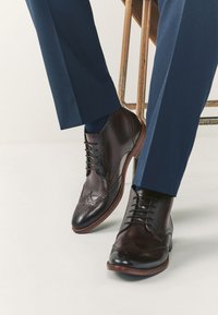 Dunkelbraune Leder-Oxfords mit Brogue-Details, versehen mit einer glatten Oberfläche, Schnürdesign und einer hellbraunen Sohle.