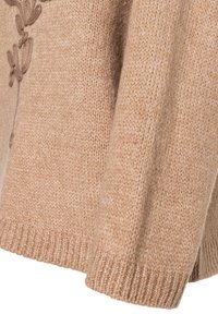 Beige gebreide trui met ribbelmanchetten, met een gestructureerd patroon aan de zijkant. Zachte stof met een iets losse pasvorm.
