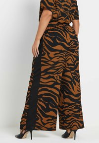 Pantaloni a gamba larga in un motivo a strisce tigre marrone e nero, realizzati in tessuto testurizzato, con vita elasticizzata e pannelli laterali a contrasto.