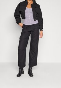 Schwarze, cropped Bomberjacke mit zwei Brusttaschen, kombiniert mit einem lavendelfarbenen, figurbetonten Oberteil und weiten, schwarzen Hosen, abgerundet mit schwarzen, heeled Boots.