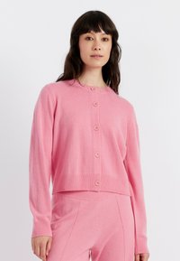 Cardigan rosa lavorato a maglia con scollo tondo, sette bottoni sul davanti e polsini e orlo a coste. Texture morbida, design cropped.