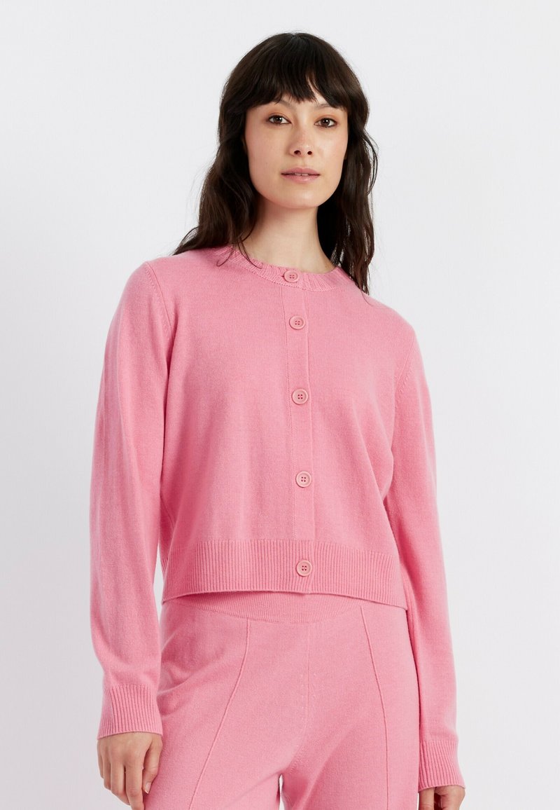 Cardigan rosa lavorato a maglia con scollo tondo, sette bottoni sul davanti e polsini e orlo a coste. Texture morbida, design cropped.