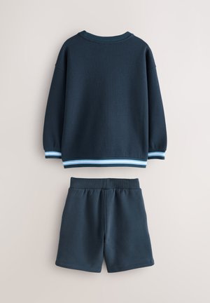 Sweat-shirt en maille bleu marine avec poignets et ourlet côtelés, orné de rayures bleu clair. Associé à un short uni bleu marine assorti, taille élastiquée.