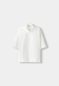 Bílá košile s krátkými rukávy zdobená složitou výšivkou na přední straně, zapínáním na knoflíky a volným, hranatým střihem.