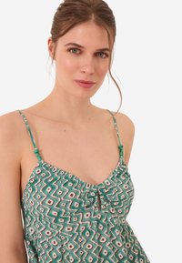 Robe à motifs verts avec des bretelles spaghetti, présentant un bustier froncé, un détail en trou de serrure et de petites perles turquoises sur les bretelles.