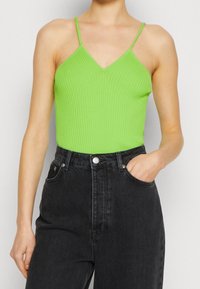 Prążkowany, jasnozielony top na ramiączkach z dekoltem w serek, zestawiony z czarnymi, wysokim stanem dżinsami z bocznymi kieszeniami i zapięciem na guziki.