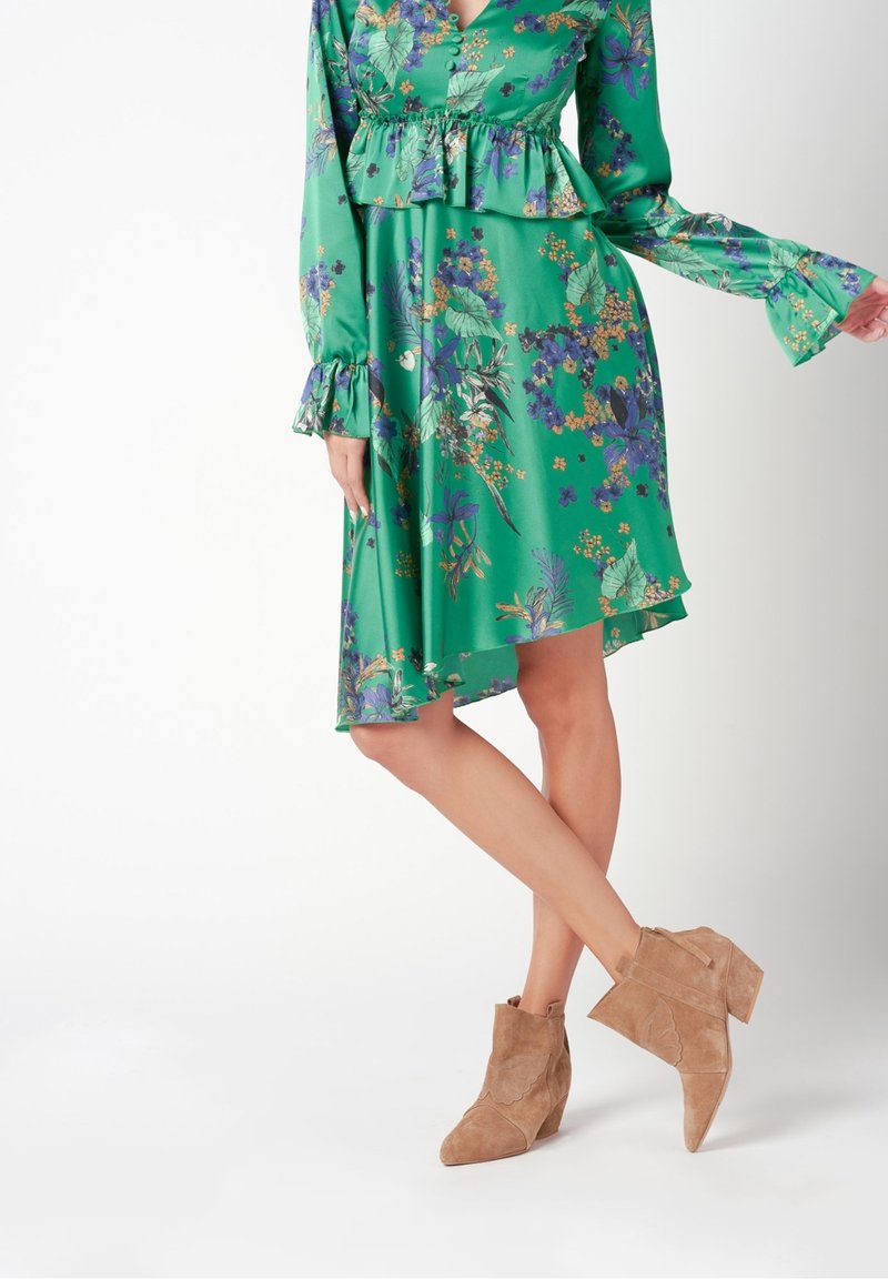 Robe florale verte avec une taille à basque, des manches longues et des poignets à volants ; associée à des bottines en suède marron clair à talon compensé.