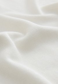Gros plan d’un tissu blanc doux avec une texture fine en maille et des plis doux, mettant en avant une surface lisse et uniforme.