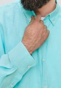 Lichtblauw, knoopsluiting shirt van linnen stof; heeft een spreidkraag, lange mouwen en zichtbare stiksels op de manchet. Handmatig de kraag aanpassend.
