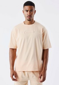 Camiseta de manga corta y cuello redondo en suave tela melocotón. Presenta un logo "PXP" elevado en el pecho. Corte relajado con una textura suave.