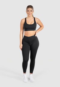 Top deportivo negro y leggings fabricados con material elástico, con un diseño sin costuras y marca mínima. Combinados con zapatillas blancas.