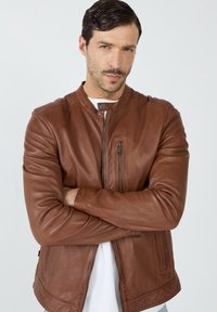Braune Lederjacke mit Stehkragen, vorderem Reißverschluss und einer Seitentasche. Glatte Textur mit minimalistischer Gestaltung.