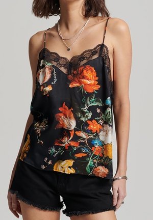 Schwarze florale Camisole mit lebhaften mehrfarbigen Blumenmustern, Spitzenbesatz entlang des Ausschnitts und dünnen verstellbaren Trägern. Kombiniert mit schwarzen Shorts.