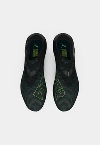 Zapatillas deportivas negras con una parte superior texturizada y acentos verdes, patrones de rayas distintivos y un diseño de corte bajo. Cintas para un ajuste seguro.