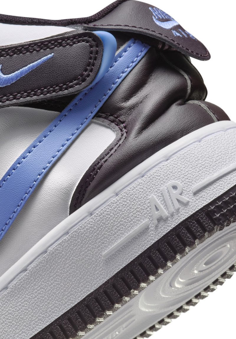 Sneakers Nike Air mają teksturowaną białą podeszwę, ciemnofioletową skórzaną cholewkę, jasnoniebieskie akcenty oraz rzep. Widoczne jest charakterystyczne logo "AIR".