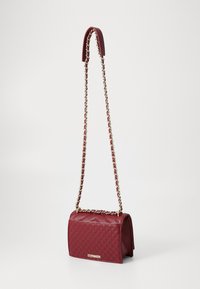 Quilted burgundy handbag with a rectangular shape, featuring a gold-tone chain strap and tag. Smooth leather texture with a structured design.