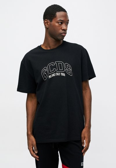 Juodas medvilnės marškinėliai su apvaliu kaklu, su baltu spaudu, kuriame rašoma "GCDS MILANO ITALY 1988" išlenktu dizainu.