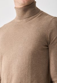 Suéter de cuello alto beige hecho de una tela suave, con un diseño ajustado y cuello acanalado, que muestra una textura suave y uniforme.