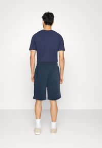 T-shirt en coton navy à manches courtes associé à un short de sudation navy avec une taille élastique et une poche latérale, porté avec des baskets claires.
