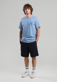 Light blue cotton t-shirt with short sleeves and a flower graphic. Worn with black shorts and white sneakers. Casual fit and design.