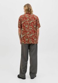 Camisa marrón de manga corta con estampado floral, combinada con pantalones grises holgados, vista desde atrás. Tejido suave, corte relajado.