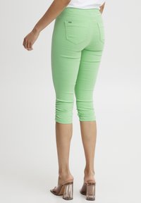 Pantalones capri verde claro con un ajuste elástico, que presentan detalles fruncidos en el dobladillo y dos bolsillos traseros, combinados con sandalias transparentes de tacón ancho.