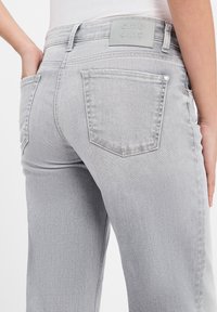 Jeans in denim grigio chiaro con vita a media altezza, tasche posteriori con dettagli cuciti e una patch in pelle grigia con logo sulla vita.