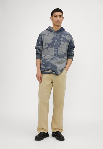 Hooded sweatshirt in gray with blue tie-dye pattern, featuring long sleeves and a front kangaroo pocket, paired with beige wide-leg pants.