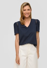 Navy V-hals t-shirt met puffed korte mouwen en gaasdetails op de schouders, gecombineerd met off-white hoge taillebroeken.