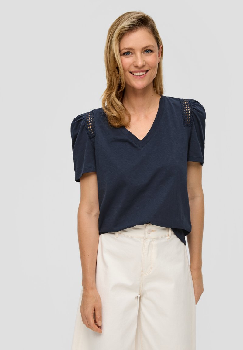 Navy V-hals t-shirt met puffed korte mouwen en gaasdetails op de schouders, gecombineerd met off-white hoge taillebroeken.