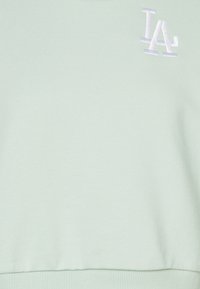 Felpa corta verde chiaro realizzata in tessuto morbido, con un logo "LA" ricamato in bianco sulla parte anteriore e un orlo a coste.