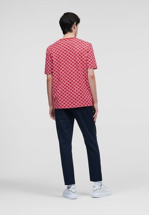 Rød kortærmet T-shirt med et geometrisk hvidt mønster, parret med marineblå bukser og hvide sneakers. Glat tekstur, afslappet pasform.