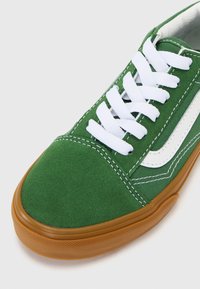 Grønne lærreds sneakers med hvide snørebånd, gummisål og kontrasterende hvid sidekant. Har syning og en tekstureret overflade.