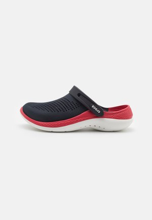 Sabot perforé bleu marine avec une accent rouge et une semelle blanche, doté d'une sangle arrière pour un maintien sécurisé et d'un design arrondi et lisse.