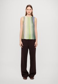 Top sin mangas multicolor con rayas verticales en verde, púrpura y plata, combinado con pantalones de pierna ancha de chevrón marrón oscuro.