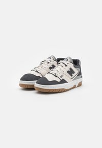 Ein Paar New Balance 550 Sneaker in Weiß und Dunkelgrau mit Gummisohlen, weißen Schnürsenkeln und Logo an der Seite, vor einem weißen Hintergrund.