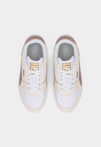 Ζευγάρι λευκά και μπεζ αθλητικά παπούτσια Puma με καφέ λεπτομέρειες, λευκά κορδόνια και χρυσό λογότυπο Puma στη γλώσσα και στις πλευρές, απεικονιζόμενα από πάνω.