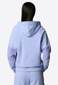 Lila hoodie med en framficka och huva med dragsko. Har färgblockerade ärmar i olika nyanser av lila. Mjuk, texturerad material.