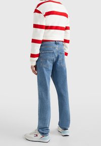 Světle modré džíny s rovnými nohavicemi, se zadními kapsami a jemným blednutím. Kombinované s bílým svetrem s červenými pruhy.