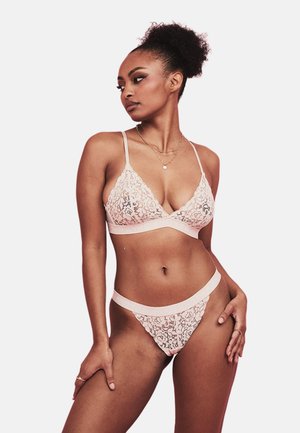 Kant bralette en string in lichtroze. Met bloemmotief, verstelbare bandjes en zachte textuur. Elastische tailleband op de string.