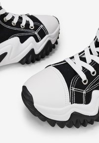 Zapatillas en blanco y negro con una suela de goma texturizada, que cuentan con una puntera blanca lisa, parte superior de lona y detalles de costura en contraste.