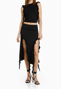 Schwarzes zweiteiliges Outfit mit einem gerafften Crop-Top und einem langen Rock mit hohen Seitenschlitzen; gefertigt aus glattem, dehnbarem Stoff.