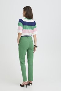 Top à manches courtes rayé en marine, vert, rose et blanc, associé à un pantalon vert ajusté et des sandales à talons noires ; design minimaliste.